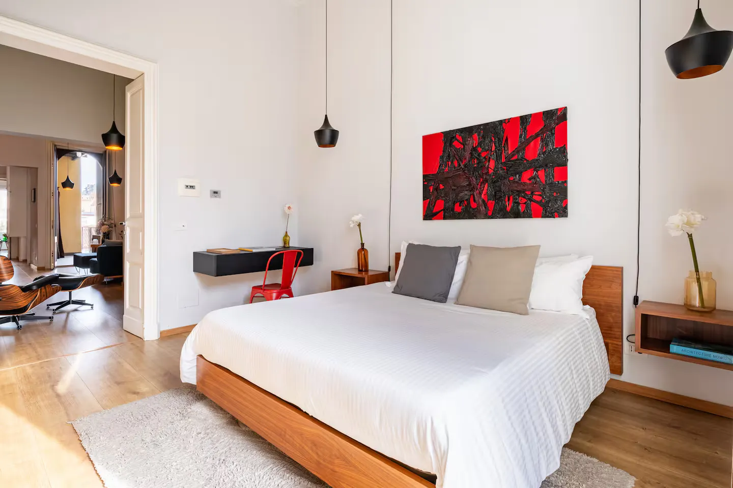 Room 01: letto in legno con testiera bassa, quadro astratto rosso e nero alla parete, lampade a sospensione nere e sedia Tolix rossa alla scrivania
