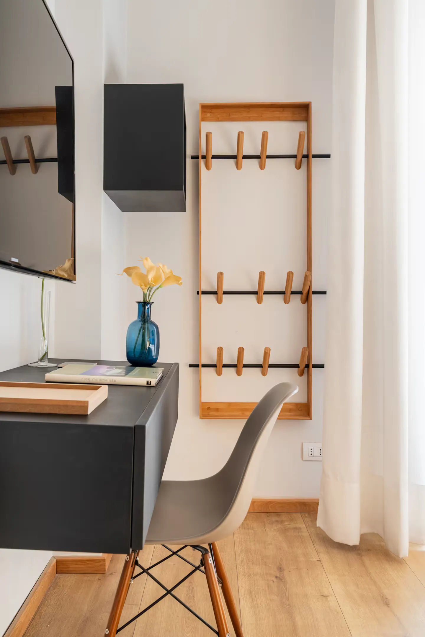 Room 02: scrivania nera a parete con vaso in vetro blu cobalto, sedia Eames e appendiabiti in legno chiaro