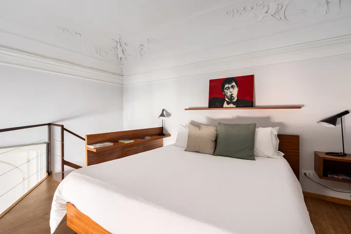 Room 04: letto con biancheria bianca e cuscini verde salvia, quadro rosso con ritratto sulla mensola alla testiera, soffitto con stucchi a volta e scala verso il mezzanino sullo sfondo